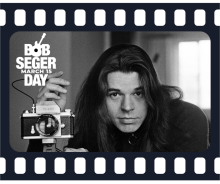 Black and white photo of a man with long hair in a dark turtleneck next to a camera on a tripod. with a filmstrip border and the words Bob Seger Day March 15