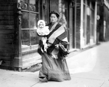 Woman and baby walking in front of a Kosher butcher shop.