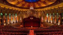 Interior of the Fox Theater in Detroit, from the perpective of the audience. Showing dark red velvet seats, Arabian inspired architechture with gold accents.