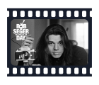 Black and white photo of a man with long hair in a dark turtleneck next to a camera on a tripod. with a filmstrip border and the words Bob Seger Day March 15