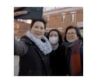 Three Aisian women taking a selfie. The woman holding the camera is wearing a black coat and a grey infinity scarf. The woman in the center of the group is wearing a mask. The third woman is wearing classes and a red and maroon scarf.