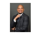 Dr. Ken L. Harris, a smiling Black man in a suit and tie posing with his hand on his chin against a gray background.