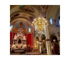 Interior of ornate catholic church with lighted crystal chandelier hanging from the painted ceiling and an altar in front of a red wall.